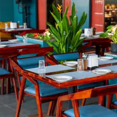 We selected furniture and a color scheme that is both bold and inviting. The contrast of the rich wood tables with the vibrant blue chairs and tropical plants contributes to the energetic and stylish ambiance of the restaurant.