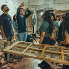 A hands-on demonstration during a Restoration Clinic workshop. An expert shows students how to assess and repair a traditional wooden door frame, bridging the gap between theory and practical craft.