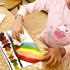 A young artist carefully painting a vibrant rainbow. The process of blending colors and the focus it requires are key benefits of our art sessions, building both skill and patience.