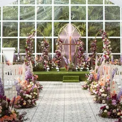 The aisle view of this stunning church-inspired wedding ceremony. The floral-lined path leads to a beautiful altar, all set against a glasshouse backdrop that brings the outdoors in.