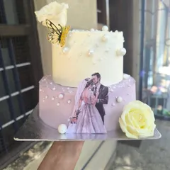 A personal and romantic two-tier anniversary cake. This design features a lovely edible print of the couple, delicate sugar pearls, and a handmade sugar flower for a truly custom touch.