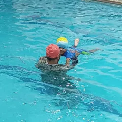 A coach provides hands-on support to a toddler, ensuring they feel secure while learning to kick in the water.