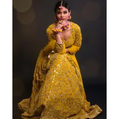 A full-length seated pose that shows the beautiful flare of the lehenga skirt. The dark background with bokeh lights adds a magical, celebratory feel.