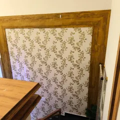 This simple yet elegant leaf-patterned wallpaper was installed within a wooden frame, creating a unique piece of wall art in a staircase area. It's a great way to highlight architectural details and add a touch of nature to transitional spaces.