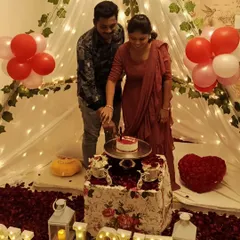 A happy couple cutting their anniversary cake inside a beautiful canopy tent I set up in their home, surrounded by rose petals, balloons, and 'LOVE' marquee letters.