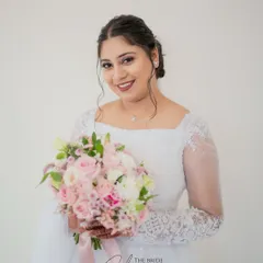 A classic bridal portrait of a Christian bride holding her beautiful bouquet of pink and white roses, looking directly at the camera with a warm smile.