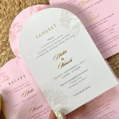 A hand holding the arched Sangeet invitation card. The combination of the unique shape, the minimalist floral illustration, and the sophisticated gold foil creates a modern and chic look.