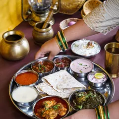 A woman's hands with traditional green bangles serving a complete Maharashtrian thali. This shot captures the essence of home-cooked hospitality and the richness of the cuisine.