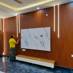 This full-wall TV unit uses vertical wood-finish louvers and integrated profile lights to create a dramatic effect. The marble-finish panel adds a touch of luxury.