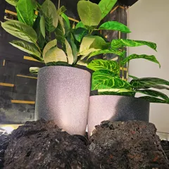 A close-up of the under-staircase pebble garden. The combination of dark pebbles, lava rocks, and high-quality artificial plants in stone-finish pots creates a sophisticated and completely maintenance-free indoor garden.
