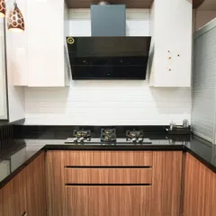A close-up of the cooking area in a U-shaped kitchen, showing the rich texture of the wood-grain laminate on the lower cabinets. The design is complemented by a black chimney and white subway tile backsplash.