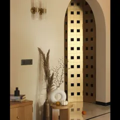 The metallic-finished mandir door, seen through an archway, creates a beautiful play of light and shadow. This custom piece acts as a spiritual and artistic focal point in the home.