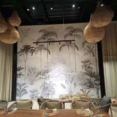 A monochrome tropical jungle mural sets a sophisticated and modern tone in this restaurant. The black and white design is timeless and pairs beautifully with the natural textures of the wicker lighting and wooden furniture.