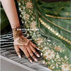 A close-up of a minimal back-of-hand design. The simple heart-shaped motif and wristband pattern complement the bride's elegant green outfit perfectly.