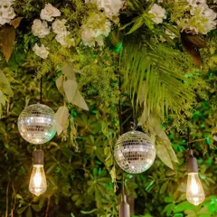 A detailed shot of the ambient lighting for a Sangeet or cocktail party. The mix of hanging Edison bulbs, small disco balls, and white flowers creates a festive and whimsical atmosphere.