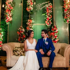 A happy couple at their reception. The backdrop features a modern design with a green wall, vertical floral arrangements, and a custom neon sign, creating a stylish and personal setting.