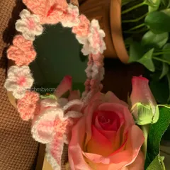 A close up shot of the crochet pink flower mirror, showing the detail of the different flower styles and the bow. It's a perfect girly accessory for a makeup table.