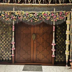 A close-up of a puja room door decorated with a full floral net of jasmine and lotus flowers. This level of detail transforms a simple doorway into a work of art for housewarming or wedding rituals.