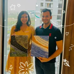 A couple proudly displays their finished textured art pieces. Each canvas tells a unique story through its colors and sculpted layers, one depicting a starry night and the other abstract ocean waves.