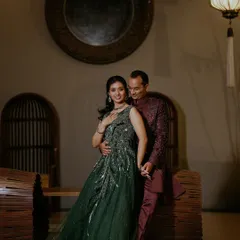 An elegant portrait of a couple in their reception attire, the bride in a stunning green gown and the groom in a complementary maroon sherwani.