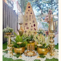 This decor for a traditional ceremony features an array of polished brass props, fragrant mogra and gulchadi flowers, and sacred symbols, creating an atmosphere of devotion and beauty.