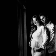An intimate black and white maternity portrait of a couple. The soft window light and close embrace create a feeling of warmth and anticipation as they await their new arrival.