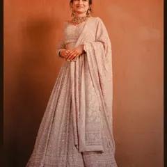 A classic, full-length studio-style portrait of the bride. The warm lighting enhances the rich texture and color of her beautiful engagement lehenga.