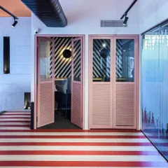 Playful design elements like these pink louvered doors and striped flooring define the private phone booths. These details add a pop of color and personality, making even the most functional spaces feel unique.