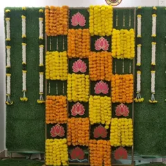 A vibrant backdrop for a Half Saree function, featuring a checkerboard pattern of yellow and orange marigolds on a green grass wall, accented with lotus cutouts.