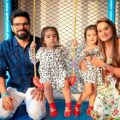 A beautiful family portrait taken in our play area. The parents are all smiles as their two little girls enjoy the swing, capturing a perfect moment of family fun.