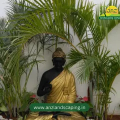 A tranquil garden corner featuring a Buddha statue nestled among palm fronds and white pebbles, creating a serene and meditative space.