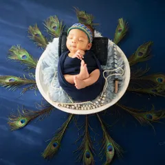 A stunning overhead shot of a newborn Krishna, surrounded by a radial display of peacock feathers on a rich blue background.