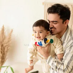 A happy father holding his son during his first birthday photoshoot. The boho studio setting provides a warm and celebratory backdrop.
