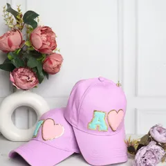 Your style, your initial. These trendy lilac baseball caps are customized with chenille initial and heart patches, making them a cute and personal accessory.
