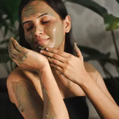 This close-up focuses on the application and texture of the mud mask. The lighting is soft and natural, emphasizing healthy, glowing skin.