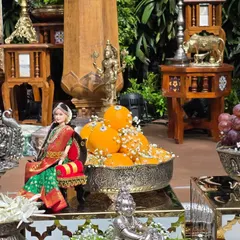 A detailed shot of an offering tray featuring a beautifully dressed doll, a bowl of oranges, and other traditional silver props.