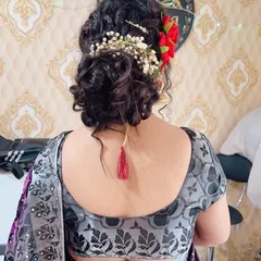A modern messy bun hairstyle, perfect for a reception or sangeet. It is decorated with a combination of fresh red roses and baby's breath.