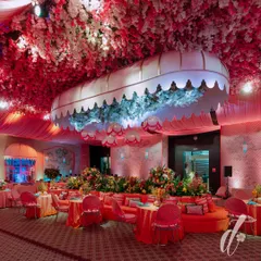 The evening look of our 'La Dolce Vita' theme, where the space was transformed with dramatic pink lighting. A custom canopy filled with blue hydrangeas became a central feature, surrounded by plush orange seating and tables set for a luxurious dinner.