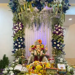 This royal Ganpati setup showcases a unique color palette of blue, purple, and white flowers. The grand arch, combined with cascading baby's breath, gives the decoration a majestic and opulent feel.