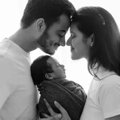 A timeless black and white portrait of new parents holding their sleeping baby. This image is pure love, capturing the profound connection of a new family.