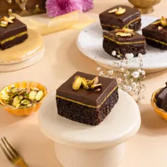 Rich chocolate and pistachio mini cakes, beautifully arranged on pedestals to give them a gourmet, artisanal feel.