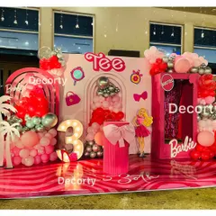 A full view of the vibrant Barbie party stage, showcasing the custom "Tee" branding and various themed icons like purses and mirrors.