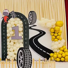 A creative backdrop for a car-themed first birthday. The design features a winding road, a number '1' filled with balloons, and tire cutouts, perfect for a little one who's ready to race into their second year.