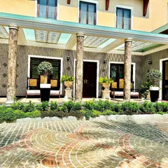 The completed entryway of the Whitefield mansion features a stunning patterned driveway and a porch framed by manicured hedges and elegant topiaries in planters. This design marries formal Mughal style with lush greenery for a truly grand arrival.