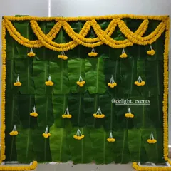 For an authentic and natural touch, we design beautiful backdrops like this one made entirely of fresh banana leaves. The simple marigold garlands and jasmine tassels make it perfect for home functions like a baby shower or pooja.