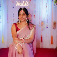 A classic portrait from a Haldi ceremony. The bride is seated gracefully against a festive backdrop, with a neon 'Haldi' sign adding a modern touch to the traditional setting.