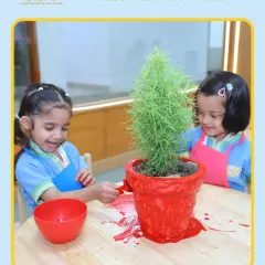 Two girls happily paint a pot together, learning to collaborate and share materials. Group art projects are great for developing social skills.