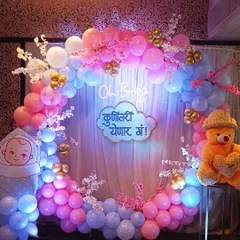 A full balloon ring decoration for a Marathi baby shower. The design incorporates the traditional 'Kunitari Yenar Ga!' sign, a teddy bear, and baby cutouts within a pink and blue balloon circle.