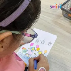 A girl wearing glasses concentrates on her coloring sheet, adding vibrant hues to a festive scene. We provide inclusive activities that allow every child to participate and shine.