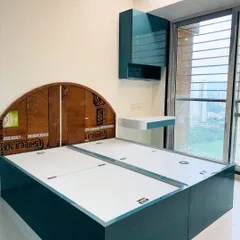 A custom bed frame in a striking teal finish, shown during the assembly process. This image highlights the sturdy plywood construction and the internal mechanism for hydraulic lift-up storage.